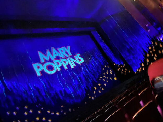 Image of the stage at Prince Edward theatre, a nighttime scene is projected onto the curtain and the words Mary Poppins feature in the centre